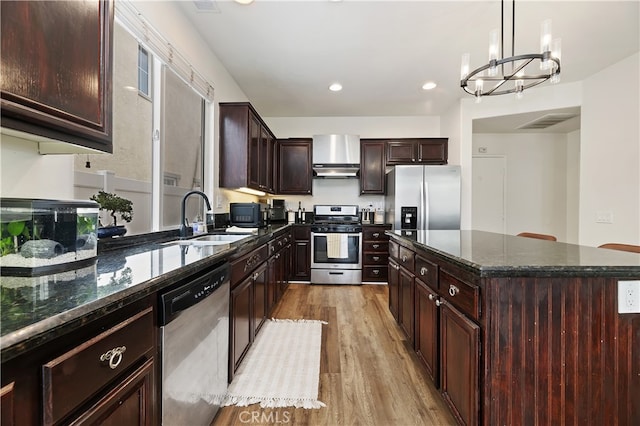 kitchen with a sink, wood finished floors, a center island, stainless steel appliances, and an inviting chandelier