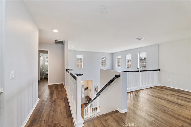 corridor featuring an upstairs landing, visible vents, baseboards, and wood finished floors