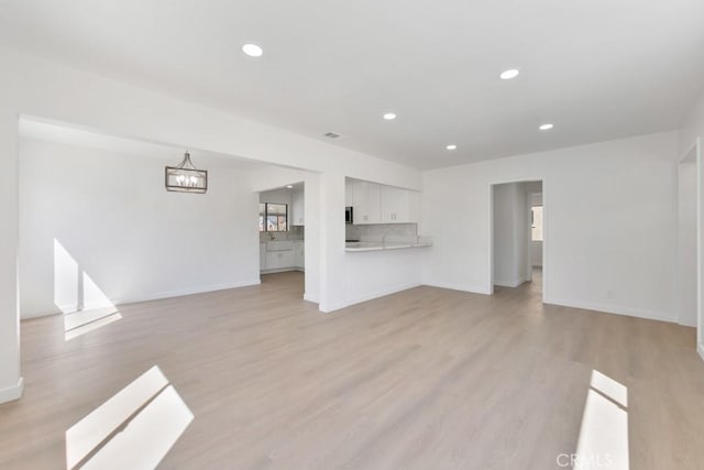 unfurnished living room featuring light wood-style floors, recessed lighting, a notable chandelier, and baseboards