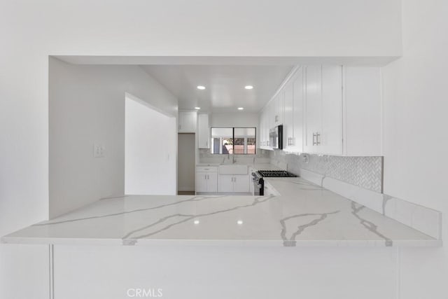 kitchen featuring a peninsula, appliances with stainless steel finishes, backsplash, and light stone counters