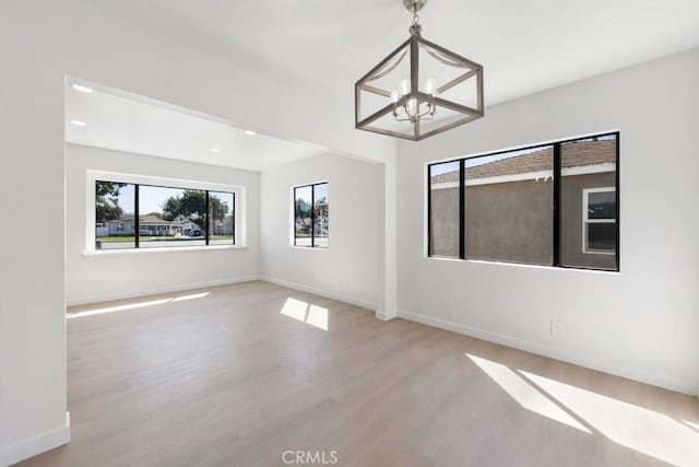 spare room with recessed lighting, light wood finished floors, baseboards, and an inviting chandelier