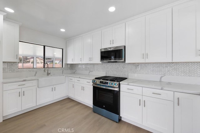 kitchen with light stone counters, stainless steel appliances, light wood-type flooring, white cabinetry, and a sink