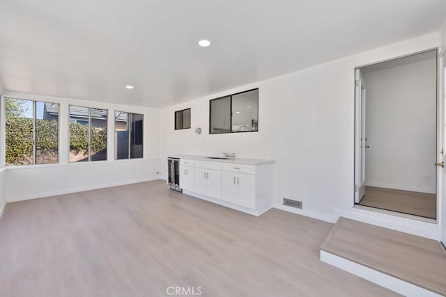 unfurnished living room with wine cooler, recessed lighting, a sink, baseboards, and light wood-style floors