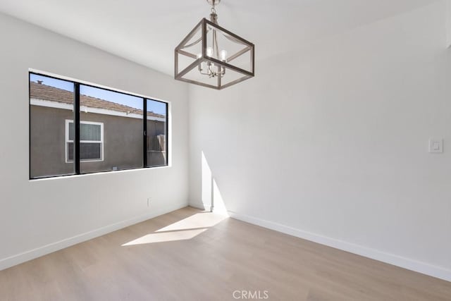 unfurnished room featuring a notable chandelier, baseboards, and wood finished floors