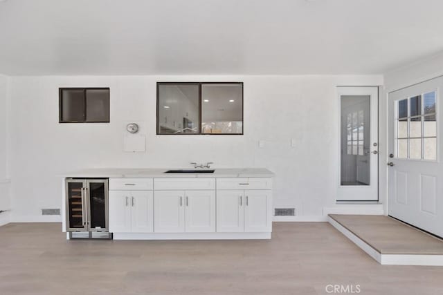 bar featuring beverage cooler, visible vents, a sink, and light wood finished floors