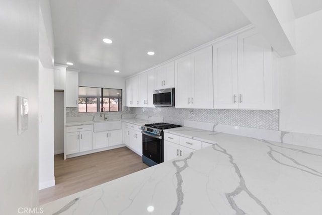 kitchen featuring a sink, white cabinets, appliances with stainless steel finishes, backsplash, and light stone countertops