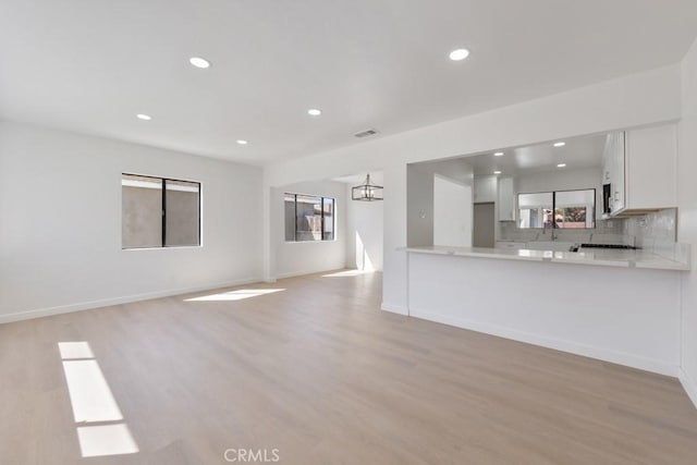 unfurnished living room with light wood-type flooring, baseboards, a notable chandelier, and recessed lighting