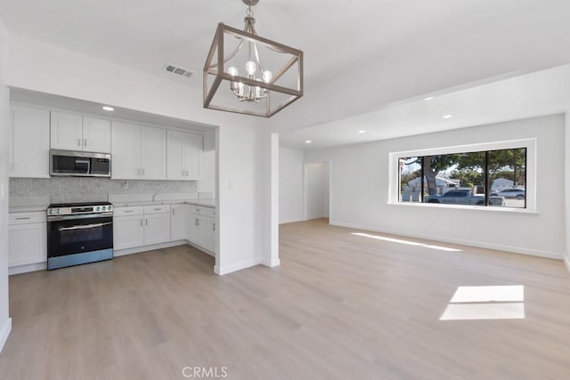 kitchen with stainless steel appliances, light countertops, backsplash, open floor plan, and white cabinets