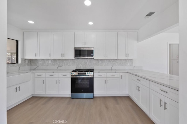 kitchen with light wood-style flooring, white cabinetry, visible vents, appliances with stainless steel finishes, and light stone countertops