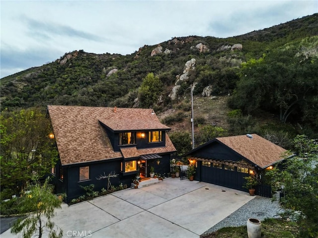 view of front of house with roof with shingles, a mountain view, and a view of trees