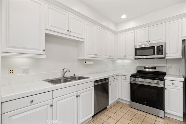 kitchen featuring tile countertops, appliances with stainless steel finishes, white cabinetry, and a sink