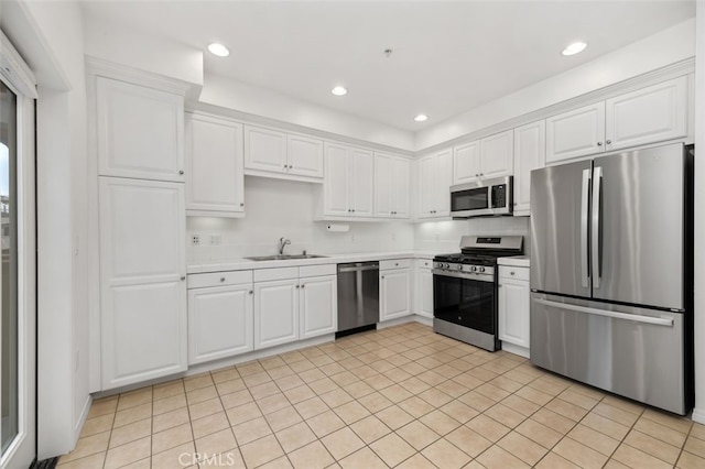 kitchen with appliances with stainless steel finishes, white cabinetry, light countertops, and a sink