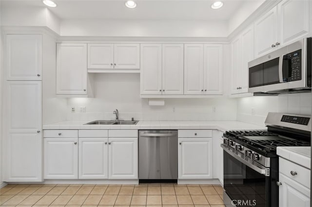 kitchen with recessed lighting, a sink, tile counters, appliances with stainless steel finishes, and white cabinetry