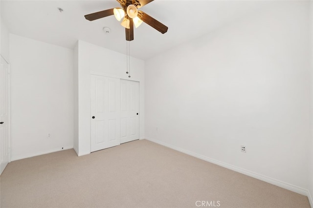 unfurnished bedroom with light carpet, ceiling fan, a closet, and baseboards