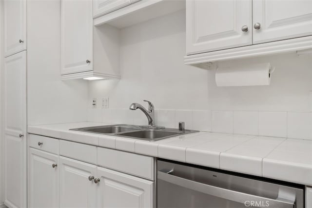 kitchen featuring tile countertops, dishwasher, white cabinetry, and a sink