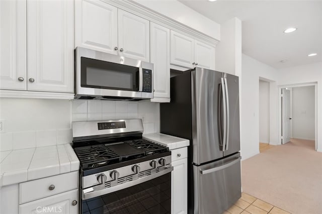 kitchen with tile countertops, stainless steel appliances, decorative backsplash, white cabinetry, and light colored carpet