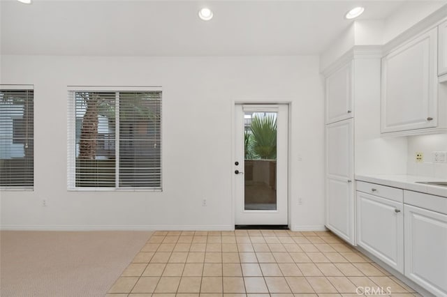 kitchen with white cabinetry, recessed lighting, light countertops, baseboards, and light colored carpet