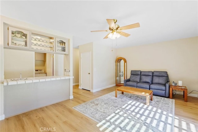 living area with light wood-style flooring, a ceiling fan, and baseboards