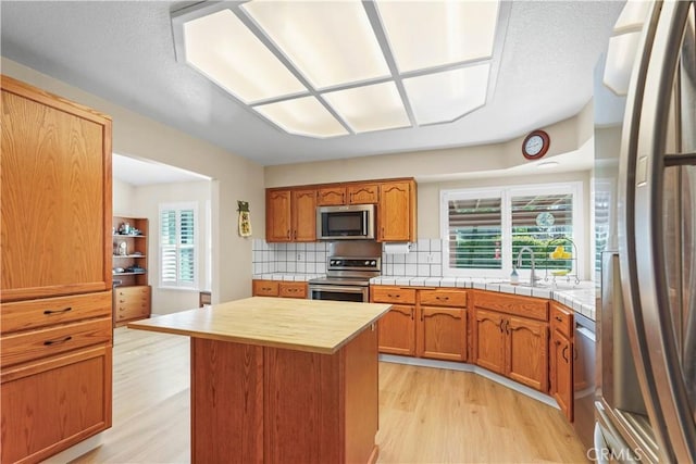 kitchen featuring tasteful backsplash, a center island, a sink, light wood finished floors, and stainless steel appliances