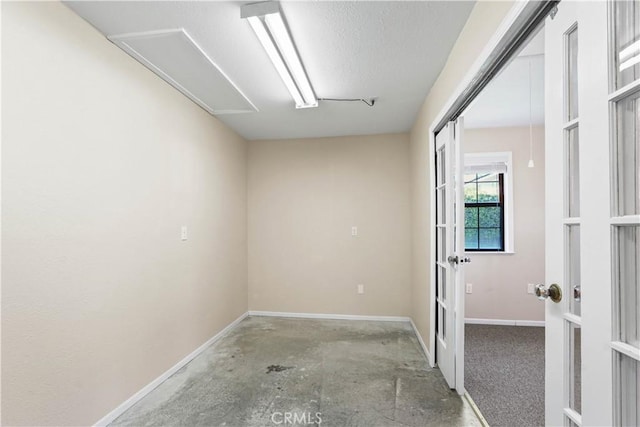 spare room with french doors, baseboards, a textured ceiling, and concrete flooring