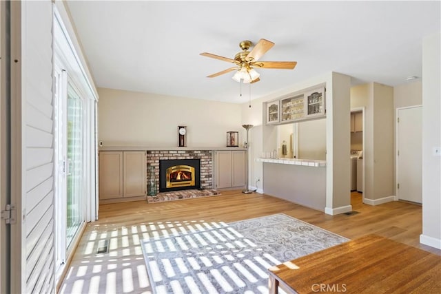 unfurnished living room with ceiling fan, baseboards, a fireplace, light wood-style floors, and washer / clothes dryer