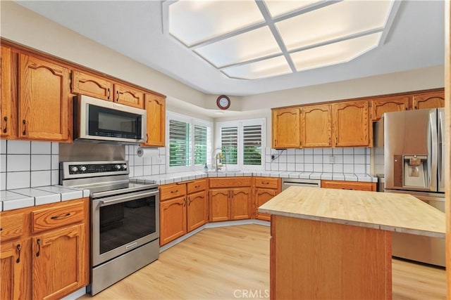 kitchen featuring a sink, light wood-type flooring, backsplash, and appliances with stainless steel finishes