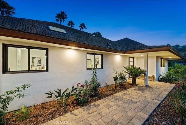 view of front of home featuring roof with shingles, a patio, and stucco siding