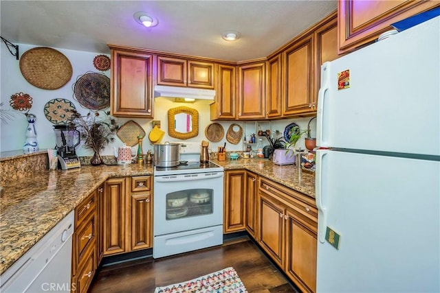 kitchen with dark wood-type flooring, white appliances, under cabinet range hood, and light stone counters