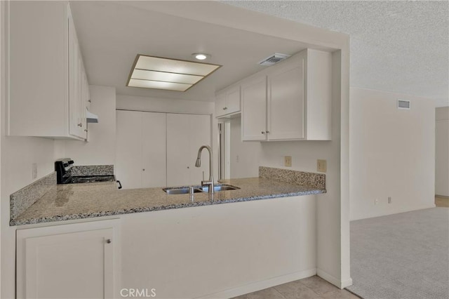 kitchen with stainless steel electric range oven, light stone countertops, a peninsula, a sink, and white cabinets