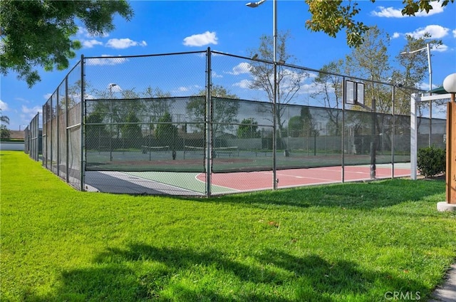 view of tennis court with community basketball court, a lawn, and fence