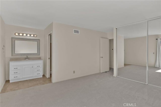 unfurnished bedroom featuring visible vents, ensuite bathroom, a sink, light tile patterned floors, and light colored carpet