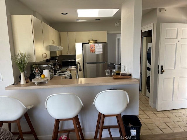 kitchen with appliances with stainless steel finishes, estacked washer and dryer, a peninsula, under cabinet range hood, and cream cabinetry