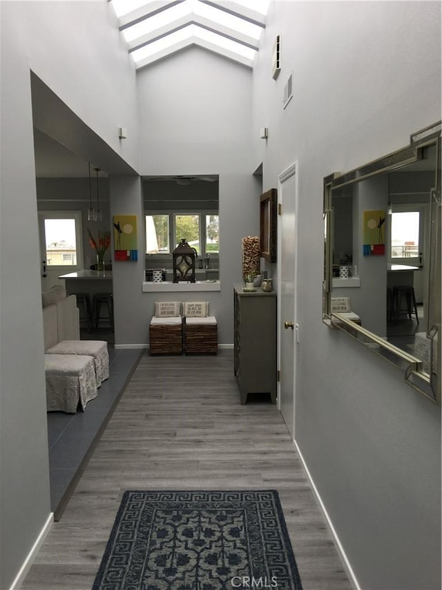 corridor with healthy amount of natural light, wood finished floors, a skylight, and high vaulted ceiling