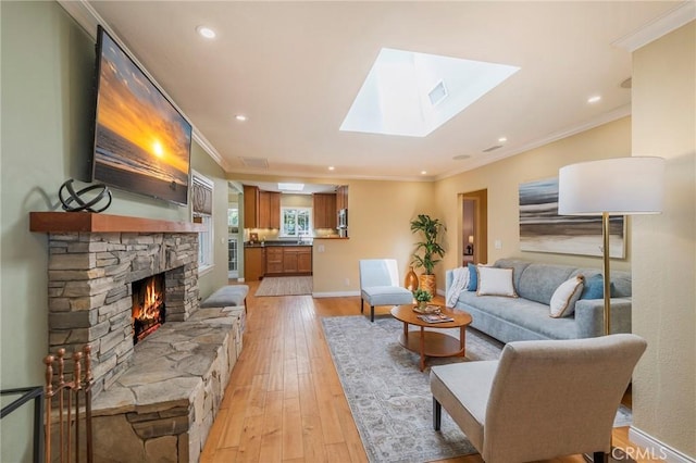 living area featuring a skylight, a fireplace, visible vents, light wood-type flooring, and crown molding