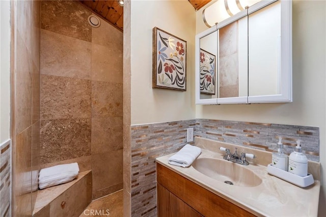 bathroom with a tile shower, a wainscoted wall, vanity, and tile walls