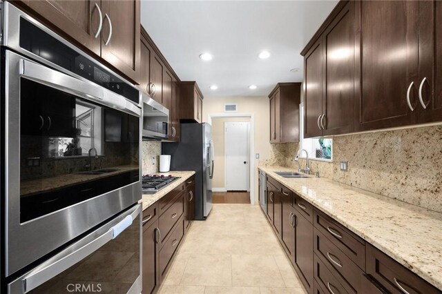 kitchen with dark brown cabinetry, light stone countertops, stainless steel appliances, and a sink