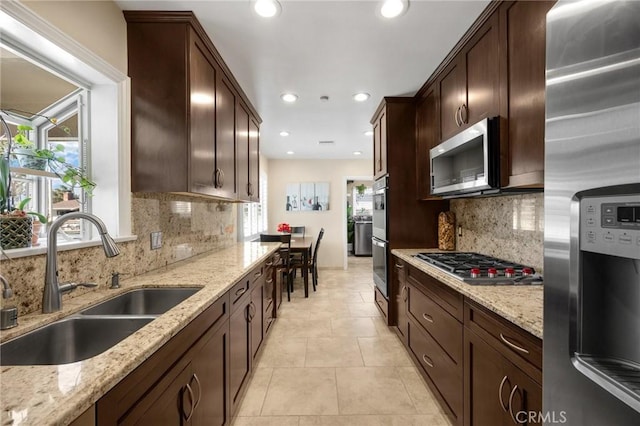 kitchen featuring a sink, light stone counters, appliances with stainless steel finishes, light tile patterned floors, and dark brown cabinets