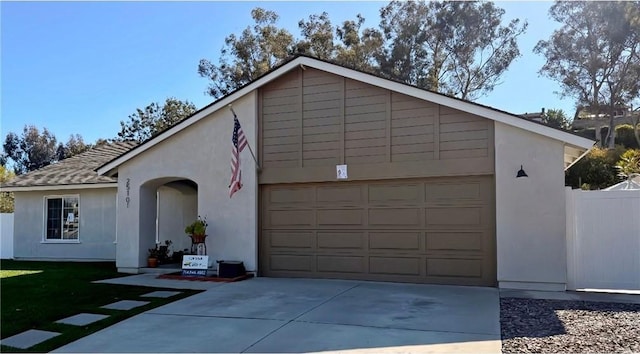 view of front facade featuring a garage, concrete driveway, fence, and stucco siding