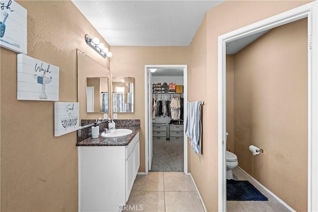 full bath with baseboards, toilet, tile patterned floors, a walk in closet, and vanity