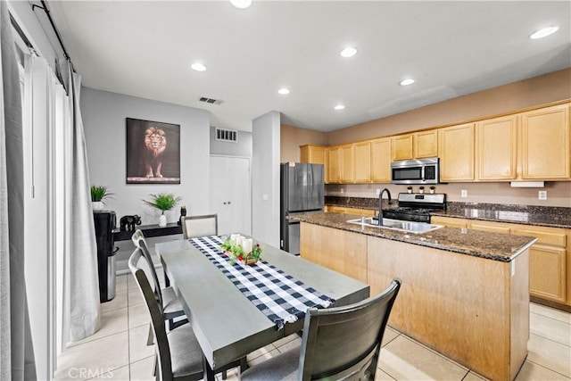 kitchen featuring stainless steel appliances, light brown cabinetry, an island with sink, and visible vents