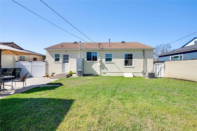 back of house with entry steps, a lawn, a patio, fence, and stucco siding