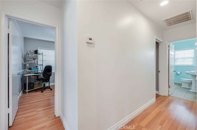 hallway featuring visible vents, light wood-style flooring, and baseboards