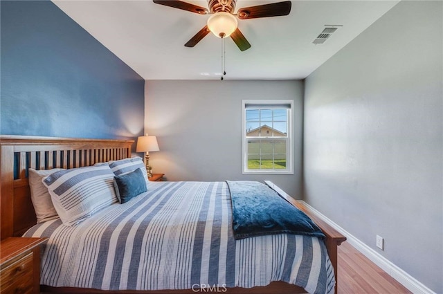 bedroom featuring a ceiling fan, visible vents, baseboards, and wood finished floors