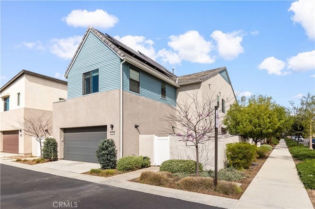 view of front of property featuring a garage, concrete driveway, fence, roof mounted solar panels, and stucco siding