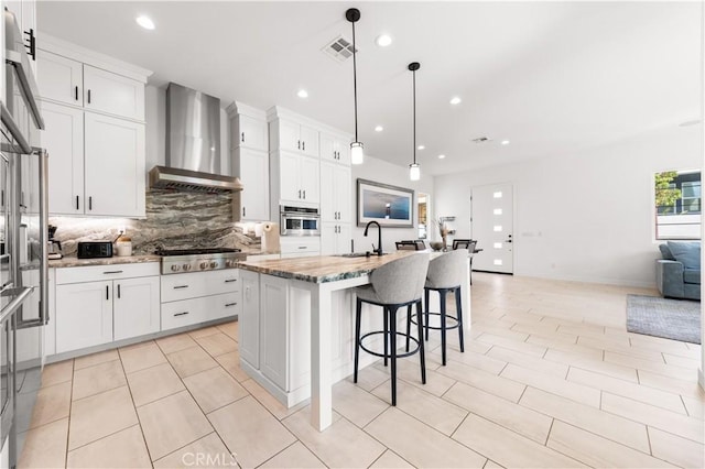 kitchen featuring a sink, open floor plan, wall chimney range hood, appliances with stainless steel finishes, and tasteful backsplash