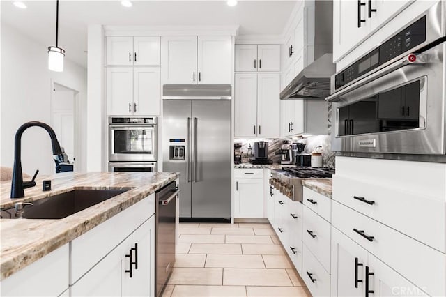 kitchen featuring wall chimney range hood, white cabinetry, stainless steel appliances, and a sink