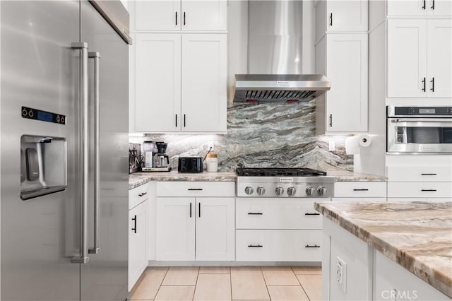 kitchen featuring light tile patterned floors, stainless steel appliances, decorative backsplash, white cabinetry, and wall chimney exhaust hood