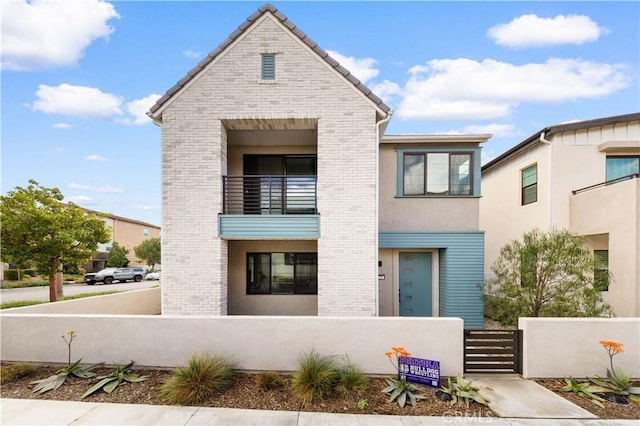 view of front of house featuring a balcony, a fenced front yard, a gate, and brick siding