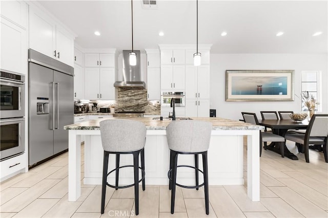 kitchen with a breakfast bar, tasteful backsplash, appliances with stainless steel finishes, a sink, and wall chimney range hood