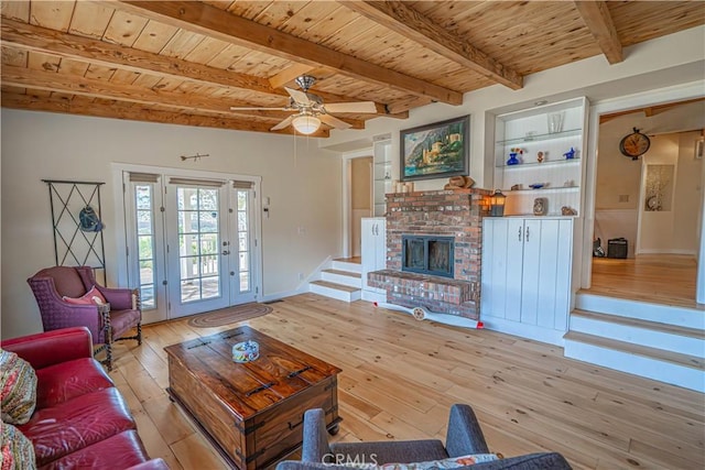 living area featuring beam ceiling, a fireplace, light wood-type flooring, wooden ceiling, and stairs